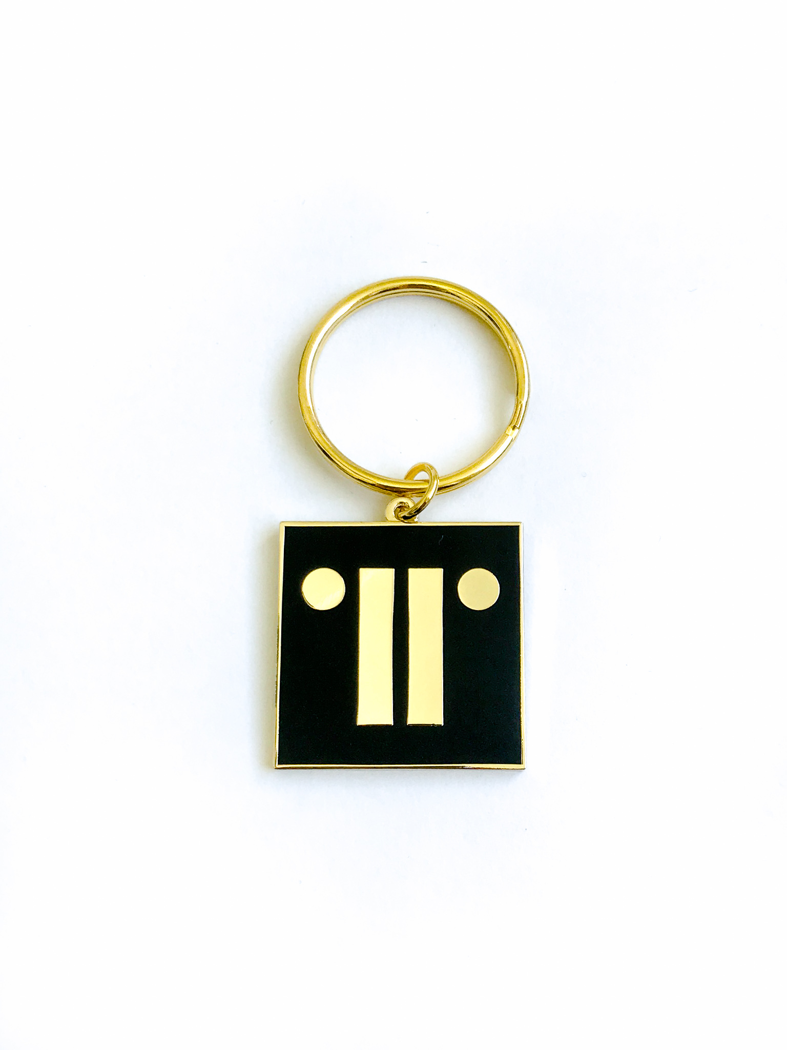 Gold keyring with black enamel paint on white background with TRG logo.