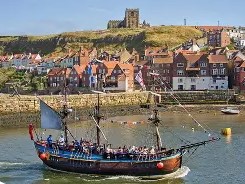 tourist boat with sails in Whitby Bay with Whitby Abbey on the hill in the background