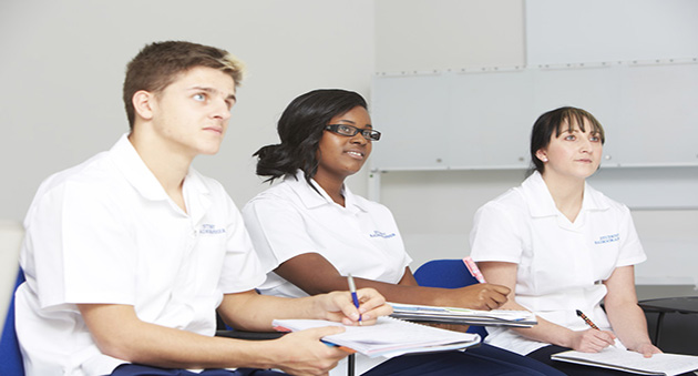 Health Studies students sat a desk learning, dressed in white healthcare uniforms