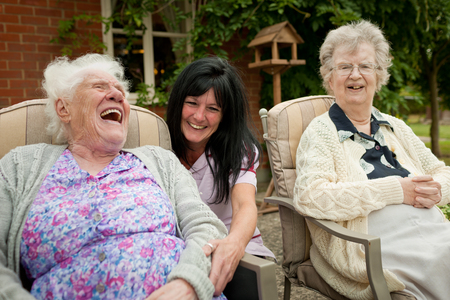 Three people sitting outdoors, smiling and enjoying a moment together in a garden setting.