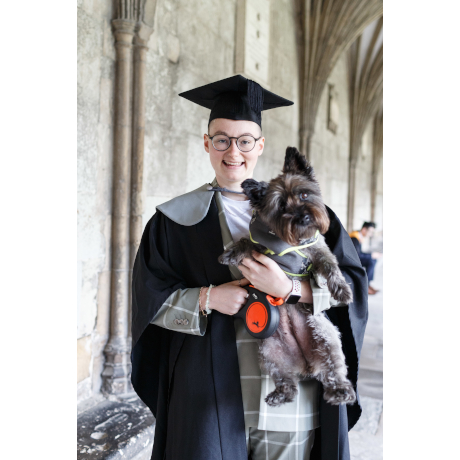 Woman wearing graduation gown and mortar board, holding a small dog