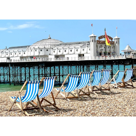 Blue and white striped deckchairs on the beach next to Brighton pier