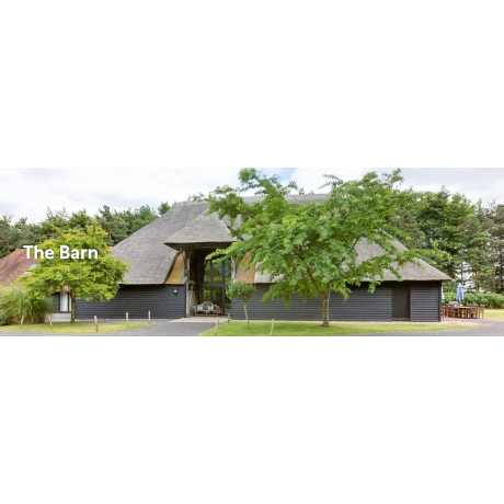 Picture of a converted barn behind green trees