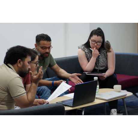 4 people in discussion with notes and a laptop.