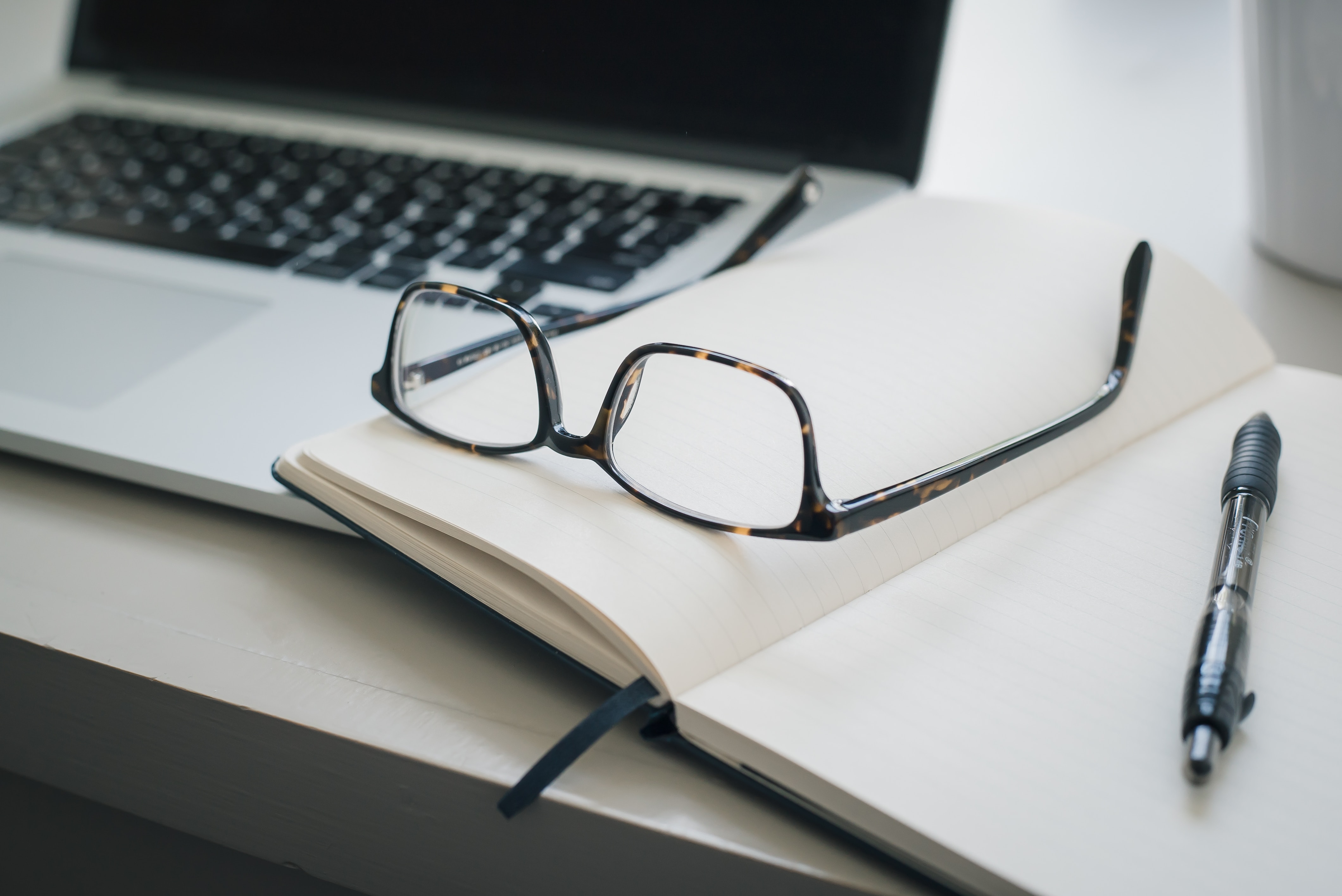 An open notebook and laptop with a pen and a pair of glasses