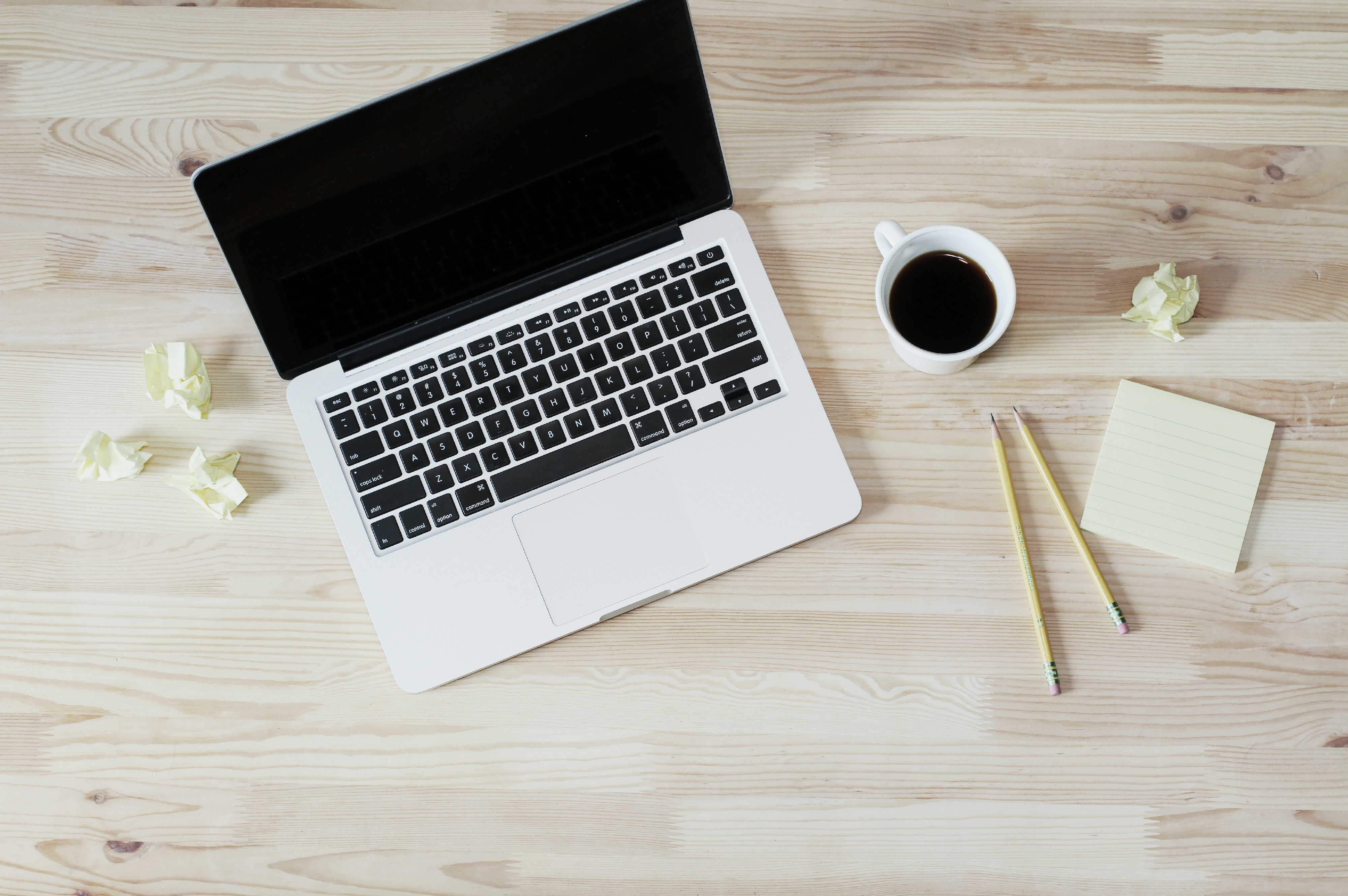 An open laptop next to a coffee cup and some sticky notes