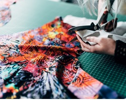 A person cutting fabric on a cutting mat with scissors.