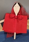 The image shows a female puppet made from a wooden stick, she is dressed in a red felt dress with a red sparkly mesh headdress.