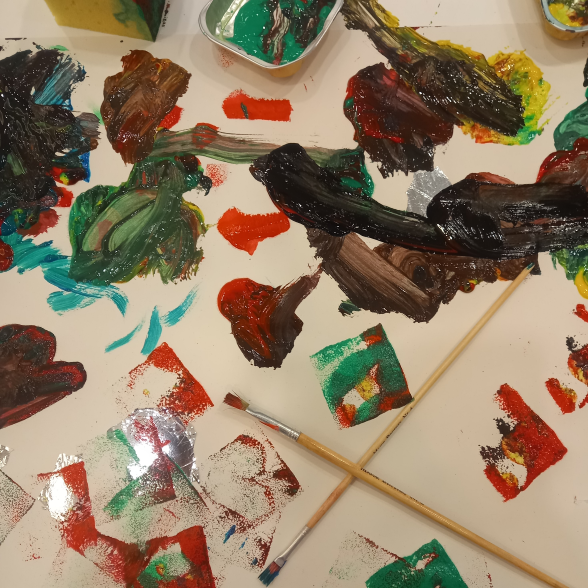 A messy table with paint brushes, paint and shiny paper