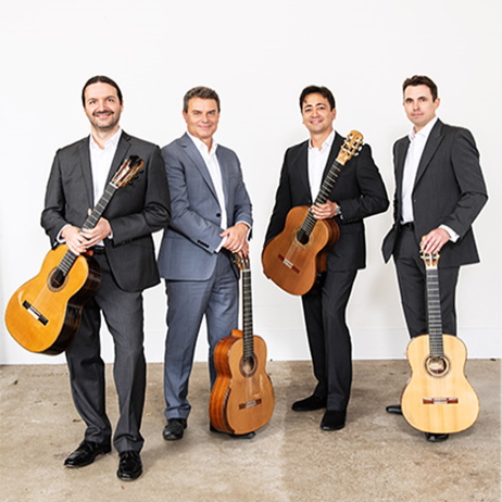 four male guitarists wearing suits and holding their guitars