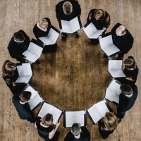 image of 12 singers in circle looking down at music image from above