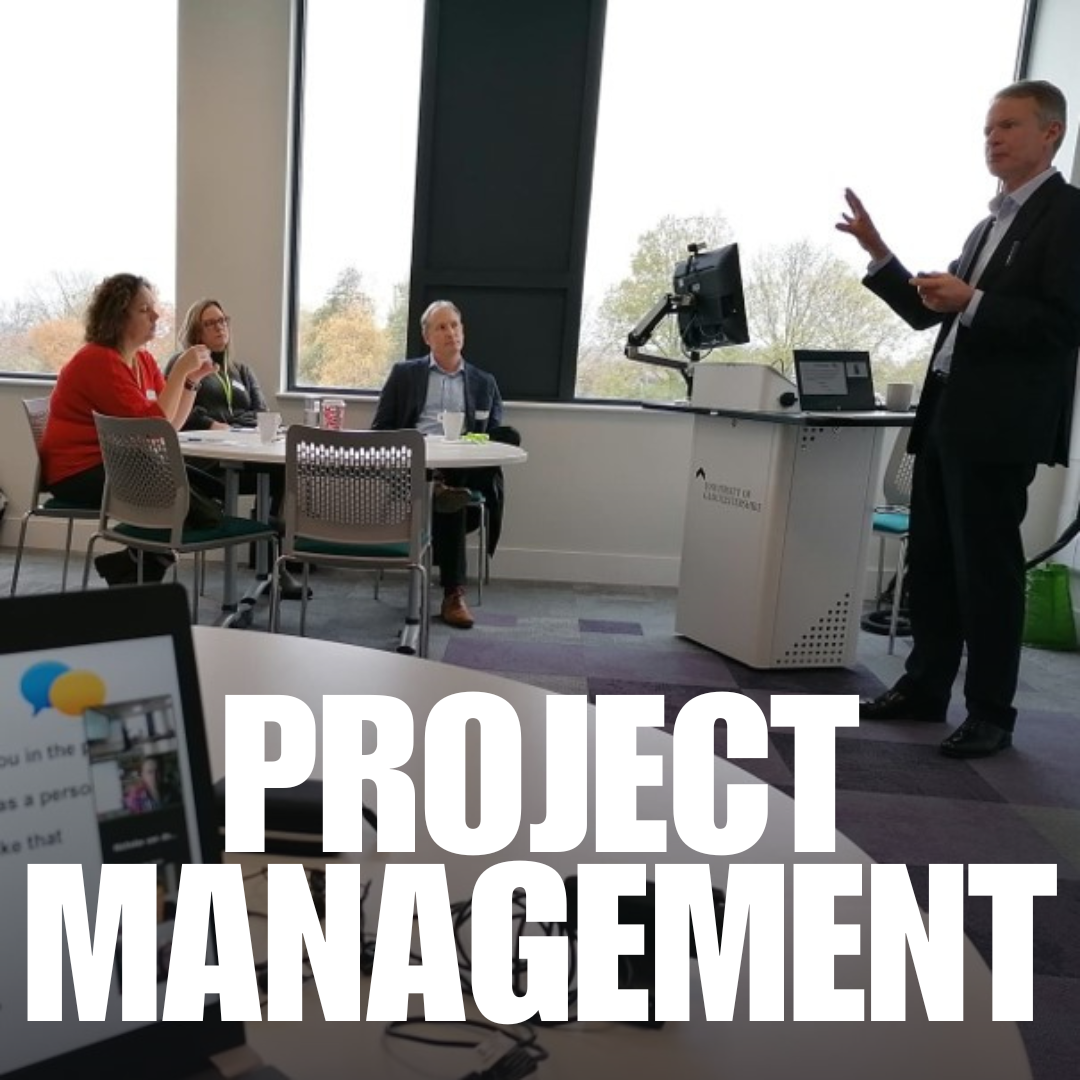 A course leader talks to a table of businesses, in the foreground there is a laptop